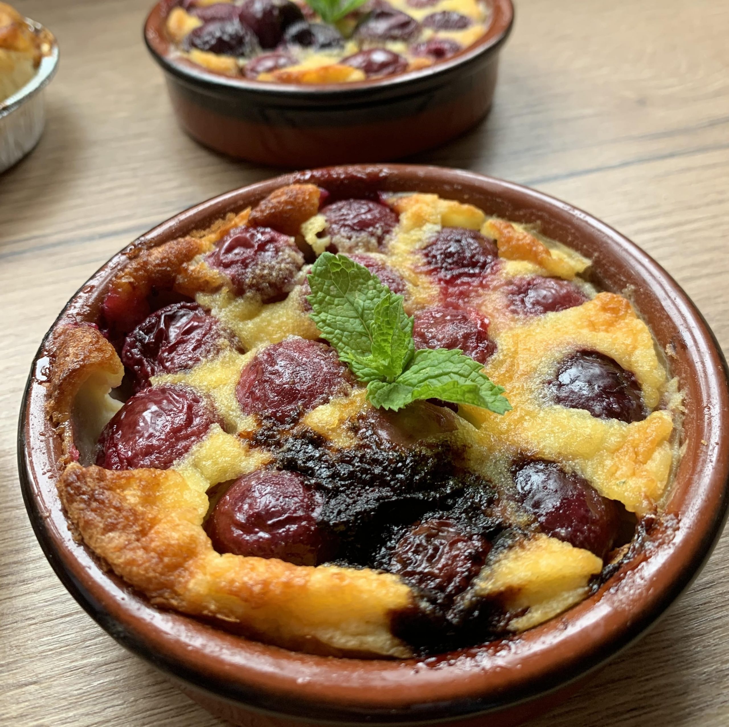 Clafoutis aux cerises servi en ramequin individuel, décoré d’une feuille de menthe