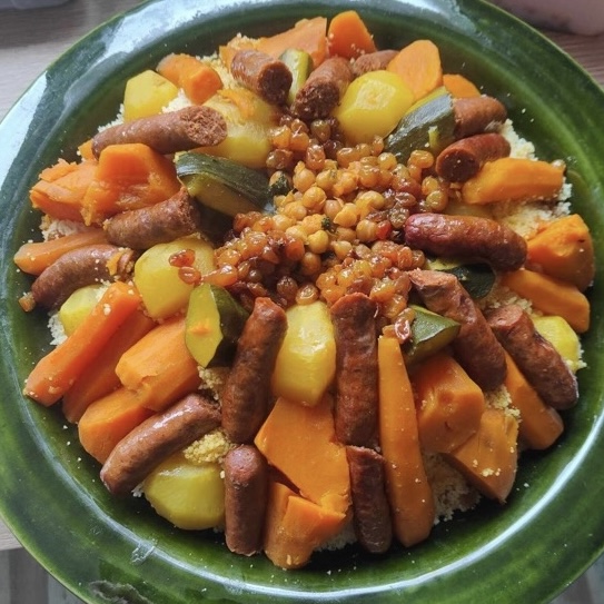 Couscous royal avec merguez, légumes variés et pois chiches dans un plat traditionnel vert